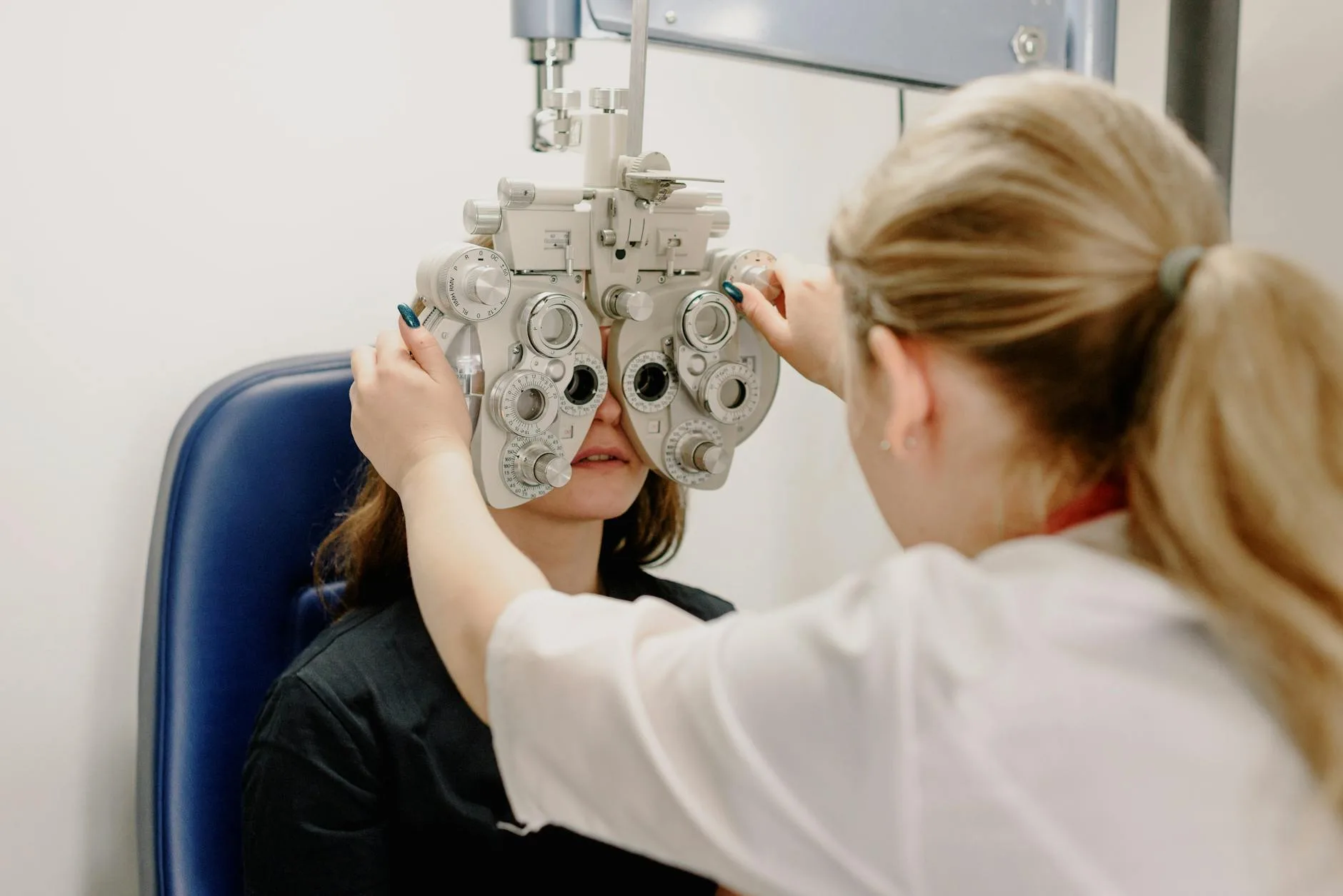 Optometrist using a phoropter for a patient's eye examination in a clinic setting.