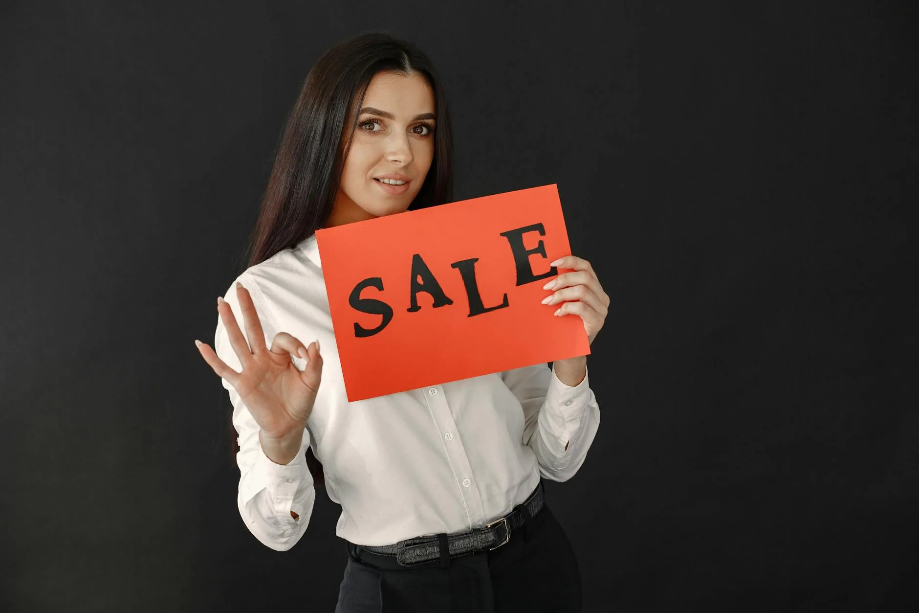Elegant woman in white shirt showing a red sale sign, ideal for promotional materials.