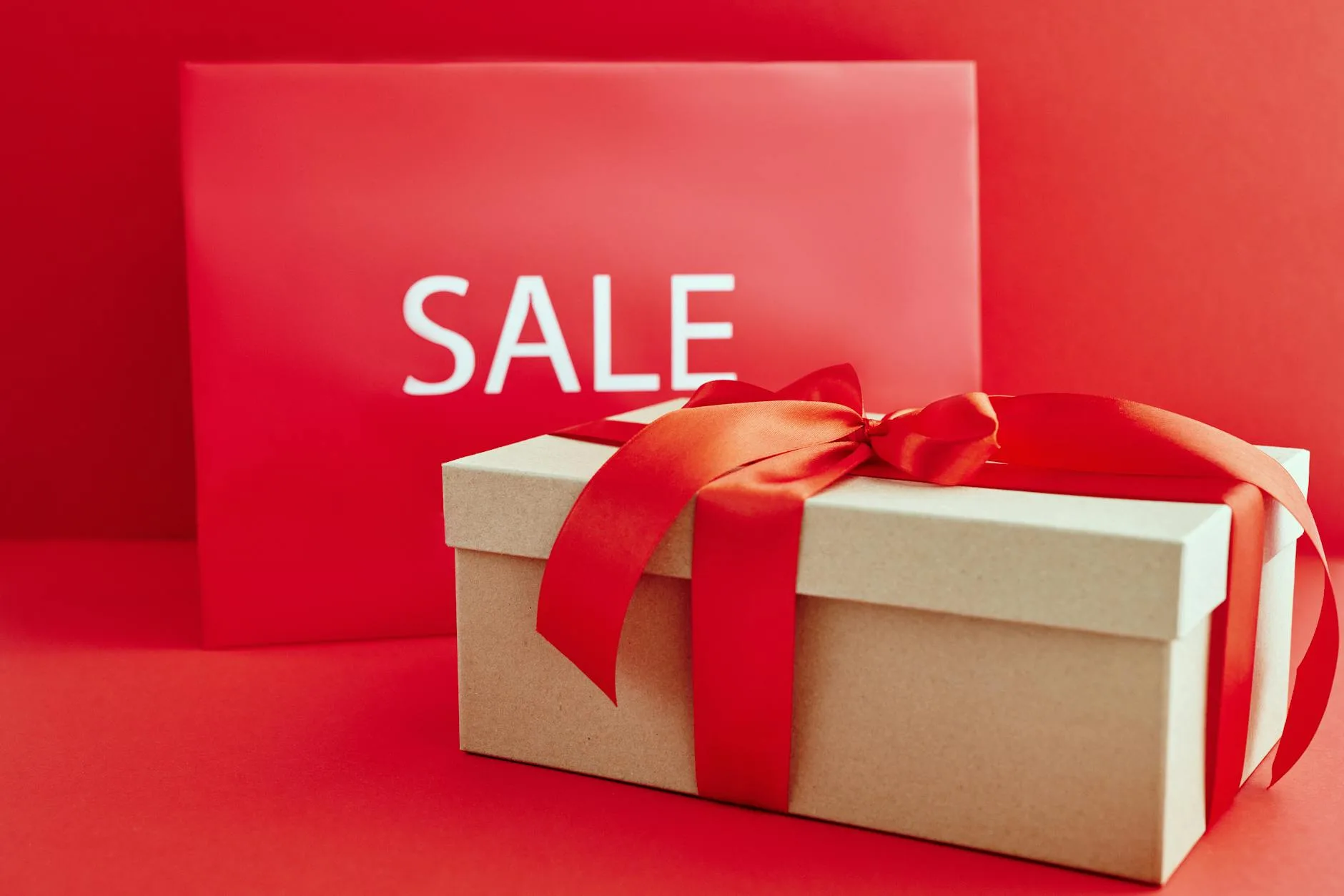 Gift box with red ribbon on red background with sale sign, perfect for retail promotions.